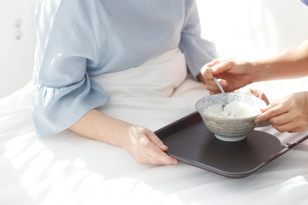 부산 암요양병원 비용|침대에 누워 있는 환자의 식사를 돕는 모습